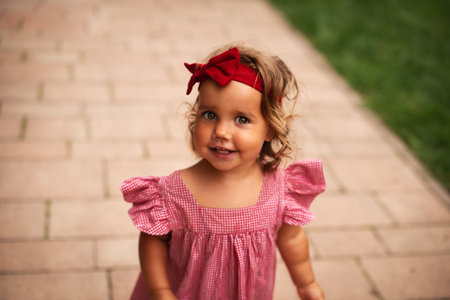Close up. Summer portrait of happy smiling baby girl in a red dress, with a red bow on her head.の写真素材
