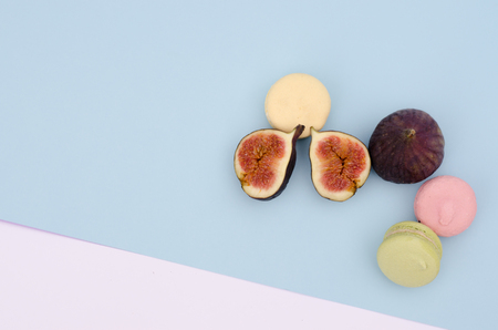 Two figs, one a host the other cut with three colourful macaroons. The background consists of two colors is blue and pink.の写真素材