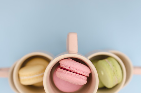 Macaroons in cups are pink, green and yellow in beige cups. The cups are exposed by the original pyramid.の写真素材