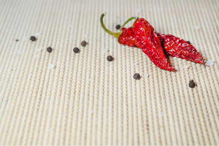 Two dried red hot pepper, sea salt and black peppercorns on a bamboo servietteの写真素材