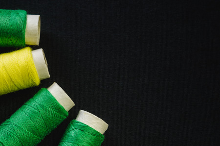 Spools of green and yellow thread on black fabricの写真素材