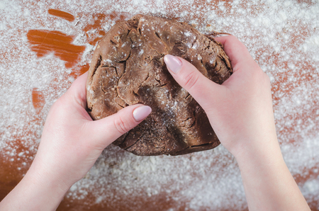 Chocolate dough for cakes in female hands on the background of a wooden board, sprinkled with wheat flourの写真素材