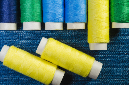 Spools of yellow, blue and green threads on a denim fabricの写真素材