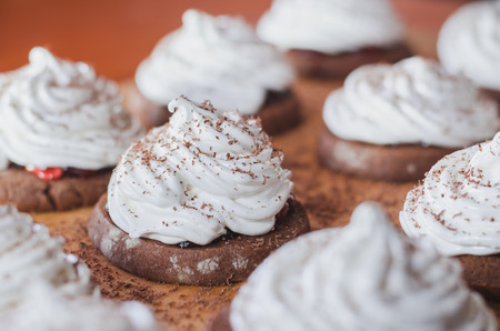 Homemade chocolate cakes with egg white cream and jam on a wooden board closeupの写真素材