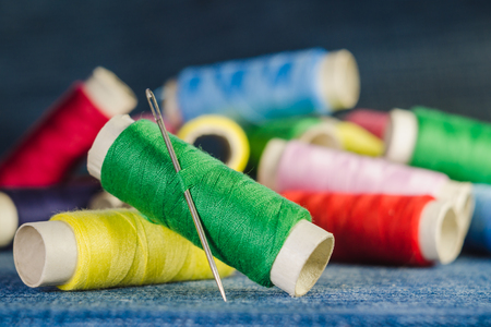Spool of green thread with a needle on the background of spools of colored threads on a denim fabricの写真素材