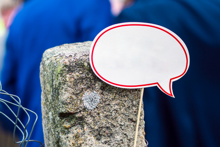 White speech cloud with copy space on a stick attached to an old concrete column on the background of people in blue clothesの写真素材