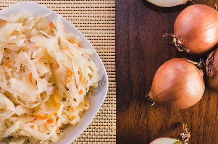 Salad of sauerkraut and carrots in a white plate and several onion bulbs on a wooden tableの写真素材