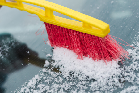 The process of cleaning the windshield of the car from the snow with a red and yellow brush