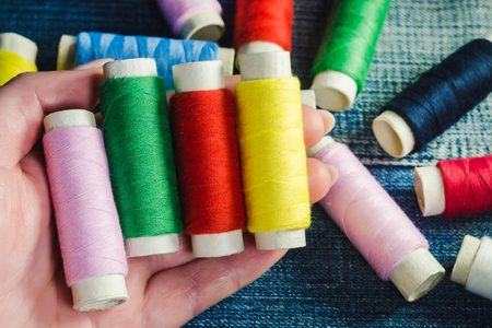 Spool of green, red, pink and yellow sewing thread  in a female hand against the background of other...