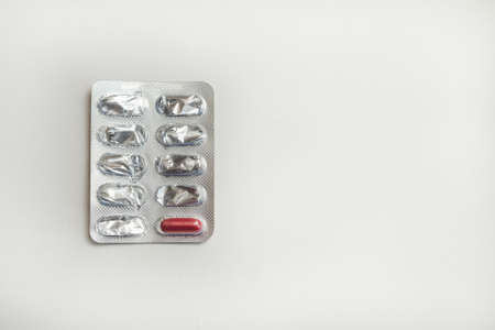 Blister with one red capsule and empty cells on a white surface with copy space.の写真素材