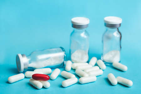 White and red capsules and glass vials against blue background, selective focus