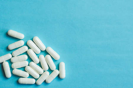 White medicinal capsules on blue background with copy spaceの写真素材