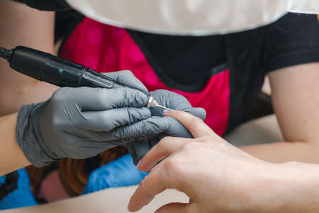 A manicurist in gray gloves treats the nail cuticle with a hardware method, close-upの写真素材