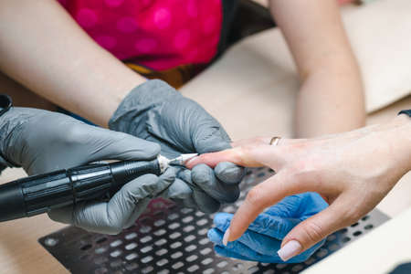 A manicurist in gray gloves cuts off an old nail covering with a hardware method close-upの写真素材