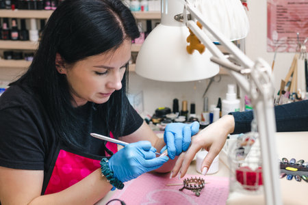 Manicurist applies a layer of gel to the nail with a brush in a cozy nail salonの写真素材