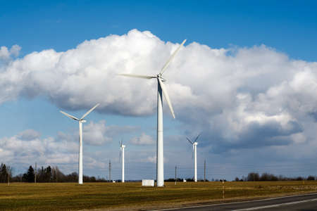 Wind turbines on a farm field against a bright blue sky with white clouds. Clean wind powerの写真素材