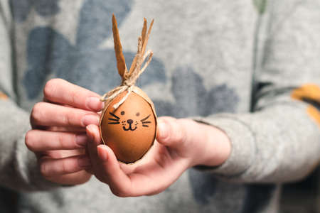 Easter bunny made from a brown chicken egg and craft paper in the hands of a girl. Happy easter symbolの写真素材
