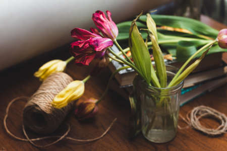 Bouquet of withered red and yellow tulips, skein of jute threads and books on an old wooden table, selective focusの写真素材