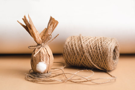Gift Easter egg in brown craft paper in the shape of a rabbit and a skein of jute threadsの写真素材
