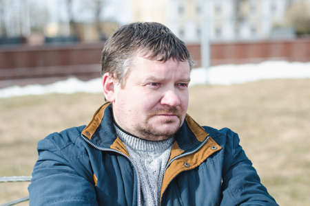 Pensive unshaven man with a sad look in a city park on a bright sunny day, close-upの写真素材