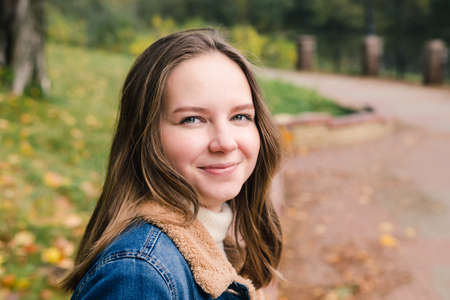 Beautiful girl with long hair in a blue denim coat in an autumn parkの写真素材