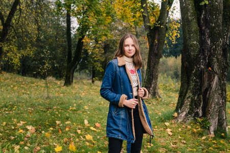 Beautiful girl with long hair in a blue denim coat in an autumn parkの写真素材
