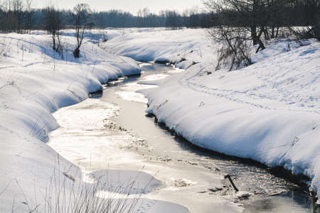 winter landscape. Small river with ice and snow-covered field on a bright sunny dayの写真素材