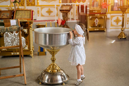 A curious girl looks into the bowl for the sacrament of infant baptism in the Orthodox church.の写真素材