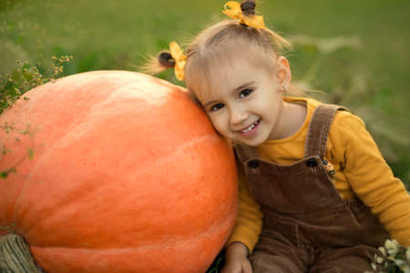 A cute little girl is sitting leaning against a huge orange pumpkin.