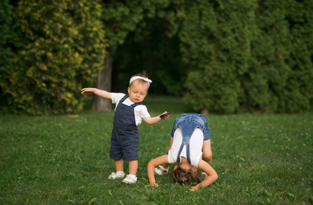 The baby takes the first steps trying to keep her balance while her sister stands on her head in the park on the lawn.の写真素材