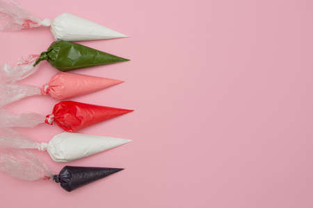 Multicolored glazing in icing bags and star shaped sprinkles on the pink table. Set for decorating...