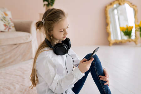 A teenage girl writes a message on her smartphone and listens to music on her headphones. Big headphones on the girl's neck.の写真素材