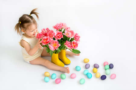 A little girl with a bouquet of tulips and Easter colored eggs on a white background.の写真素材