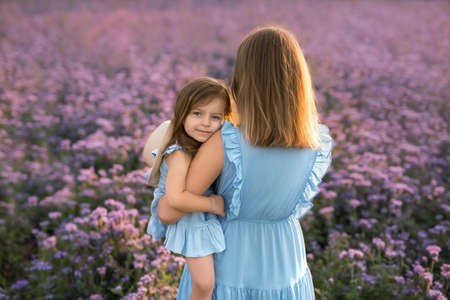 Little girl in a field of purple flowers hugs her mother tenderly. Mom holds her daughter tightly in her arms in a field of flowers.の写真素材