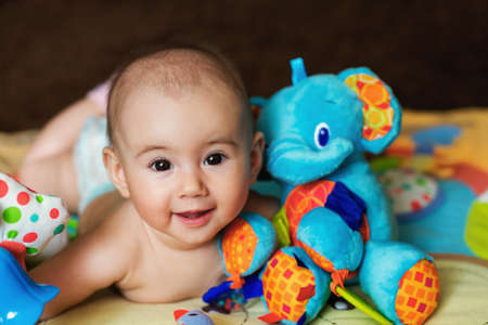 The baby is lying on his tummy hugging a toy elephant. An infant plays with toys. The child lies on the developing mat. Bright educational toys for the baby. A smile on the baby's face.の写真素材