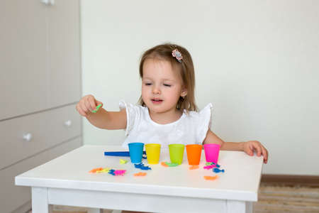 The child learns colors. A little girl sorts the animal figures by color, throwing them into the appropriate cup. Development of fine motor skills.の写真素材