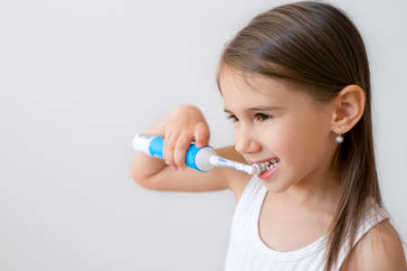 Child brushing teeth with electric toothbrush on white background. Dental hygiene. Copy space....