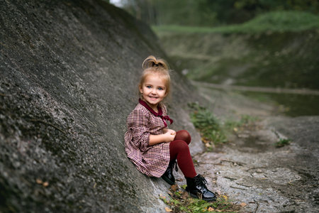 Little cute girl sitting on a rock in a rocky areaの写真素材