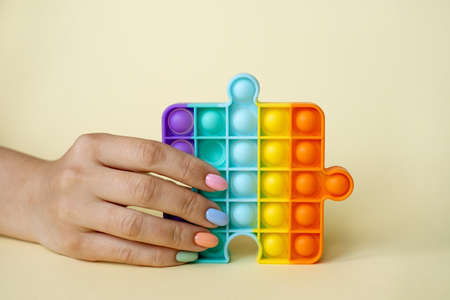 In the female hand, the popular popit toy. Anti-stress toy. entertaining games for children and adults. simple dimple. Women's nails of different colors. Colorful summer manicure.の写真素材