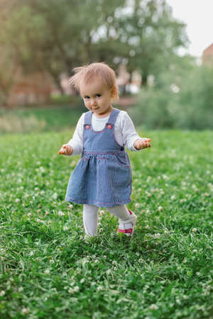 A little girl walks on the grass with her hands raised and a sly look on her face. The child takes...