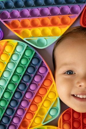 The face of a smiling child is surrounded by popular bright colorful pop it toys. A large number of popit toys. Big expressive eyes of a child. simple dimpleの写真素材