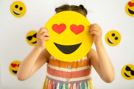 The girl is holding a happy love emoticon with hearts instead of eyes, covering her face with them. The child's face is hidden behind emojis. World smile dayの写真素材