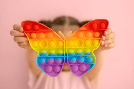 The girl is holding a bright colorful popping toy in the shape of a butterfly. A toy butterfly on a pink background. Children's educational gamesの写真素材