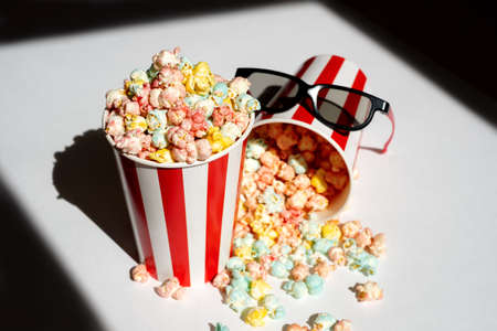 Colorful popcorn in round cardboard striped glasses with 3d glasses for fun watching movies. Shadows...