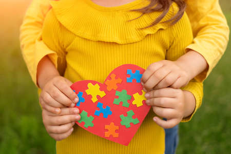 Two sisters are holding a red heart with colorful puzzles inside, made with their own hands as a sign of support for children with autism. World Autism Awareness Day. handmadeの写真素材