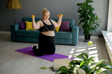 Home fitness classes and Pilates workouts, online classes at home. An overweight woman exercises under the supervision of a personal trainer. A pregnant woman watches workouts online on her laptop.の写真素材