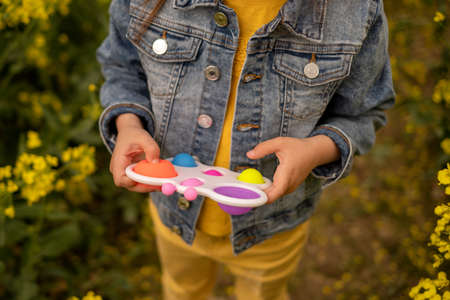 A child holds a popular simple dimple toy in a rapeseed field. Useful toys for the development of fine motor skills of the hands. Anti-stress toy. entertaining games for children. Popit toyの写真素材