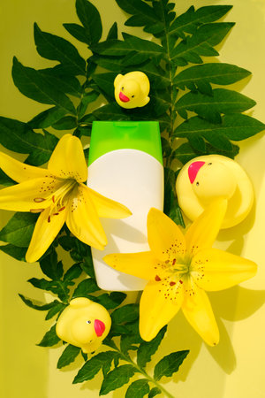 A means for bathing in a white bottle against the background of tropical plants, yellow lilies and toy ducks for the bathroom.の写真素材