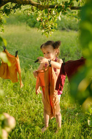 A little girl hangs clothes to dry after washing on a clothesline in nature in the fresh air.の写真素材