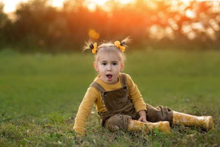 A little girl is sitting on the ground on an autumn evening at sunset with her mouth open with delight and surprise. The child is happy about the seasonal autumn sales on the market.の写真素材